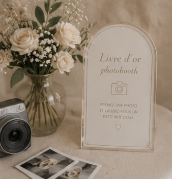 Livre d'or photobooth avec panneau d'instructions, appareil photo instantané et composition florale pour un mariage bohème.